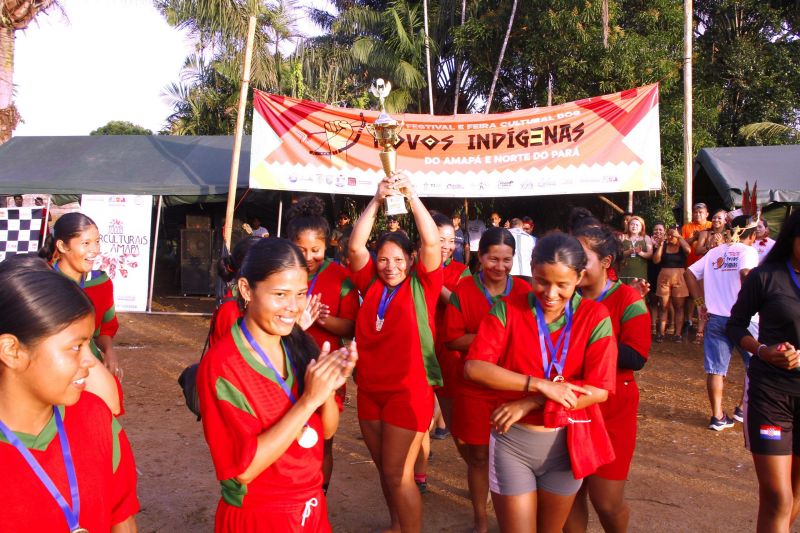 Ingrid segura a taça, campeã dos jogos de futebol e corrida com tora de madeira